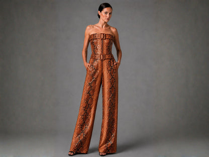 A woman modeling a strapless wide-leg jumpsuit with a brown and black snakeskin pattern and matching belt, photographed against a neutral gray studio background.