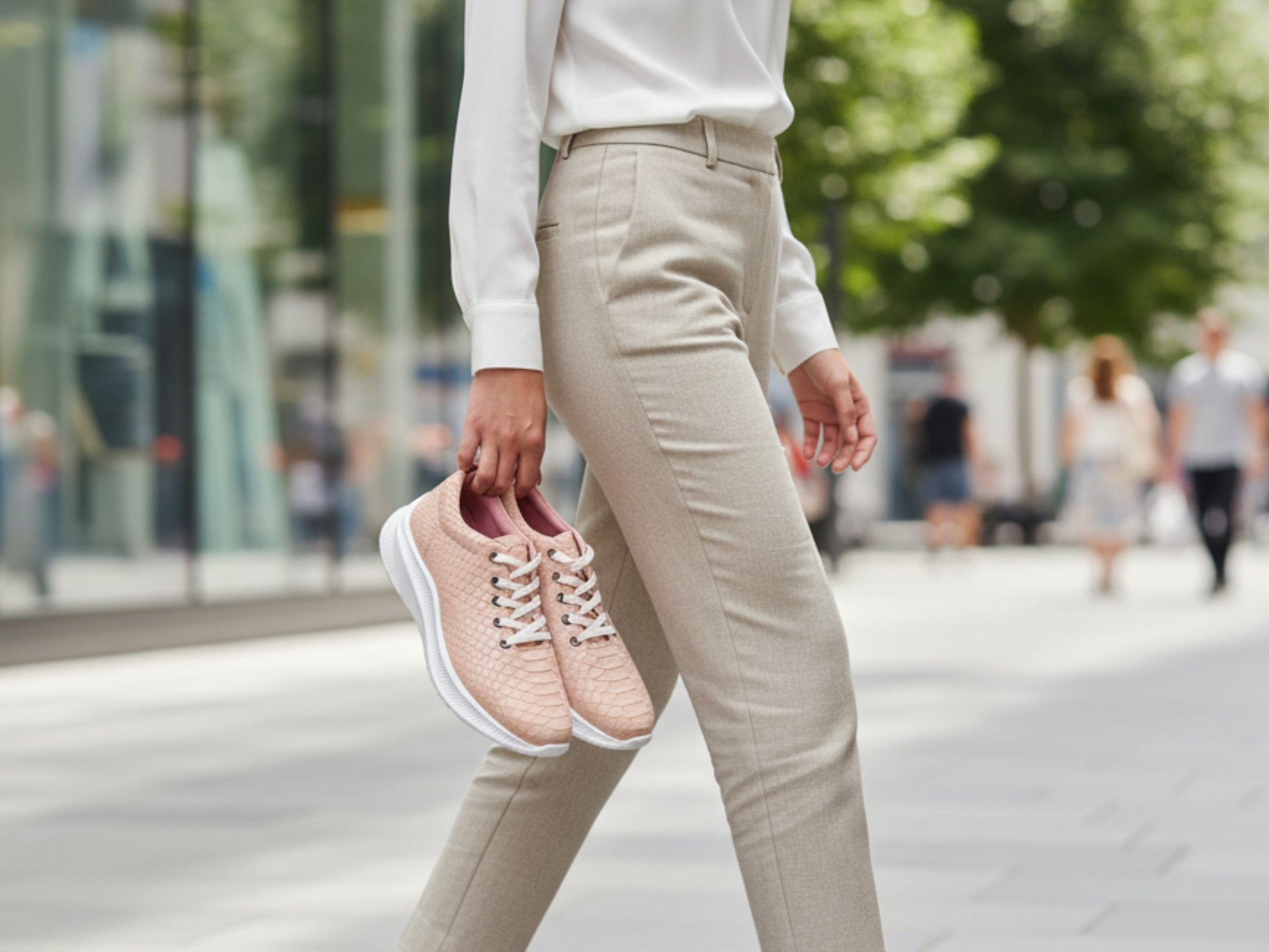 Person wearing light pink sneakers and beige pants on a city street.