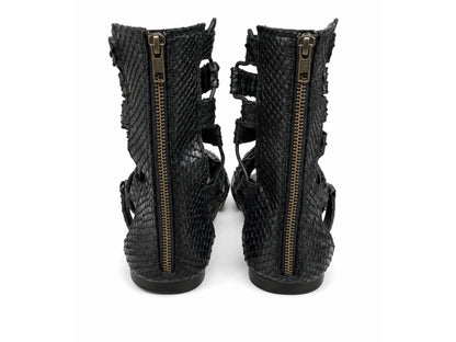 A pair of black snakeskin-textured ankle boots with side zippers and cutout straps, shown from the back against a white background.