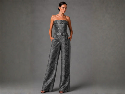A woman models a strapless wide-leg jumpsuit with a gray and black snakeskin pattern and matching belt, standing against a textured gray studio backdrop.