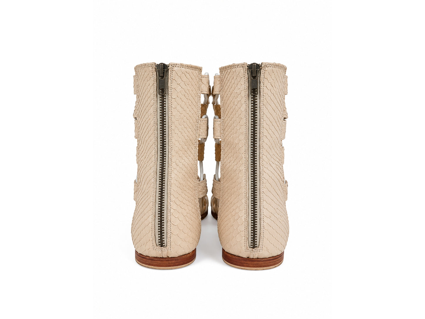 A pair of beige textured ankle boots with side zippers and decorative straps, shown from the back on a white background.