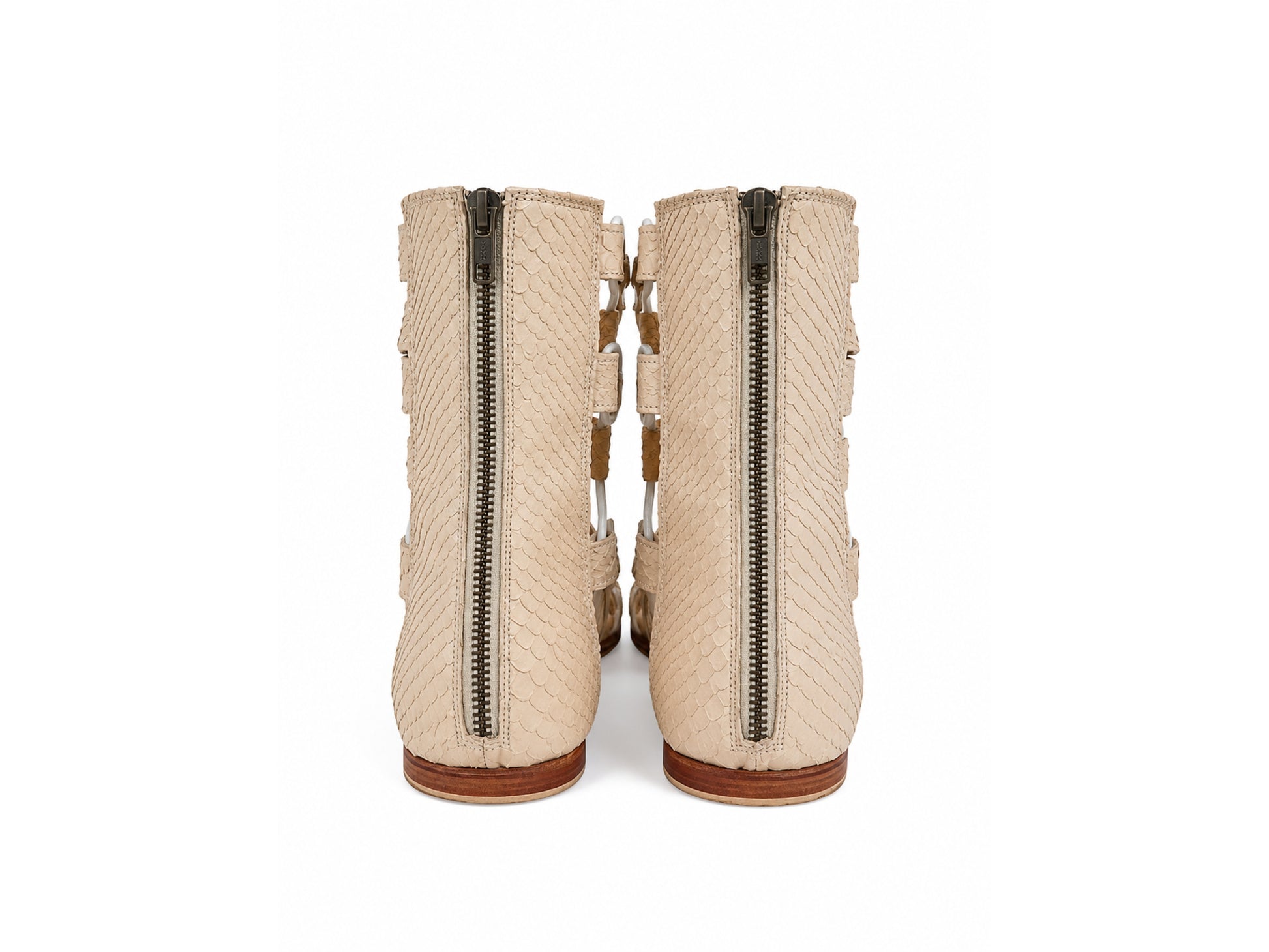 A pair of beige textured ankle boots with side zippers and decorative straps, shown from the back on a white background.