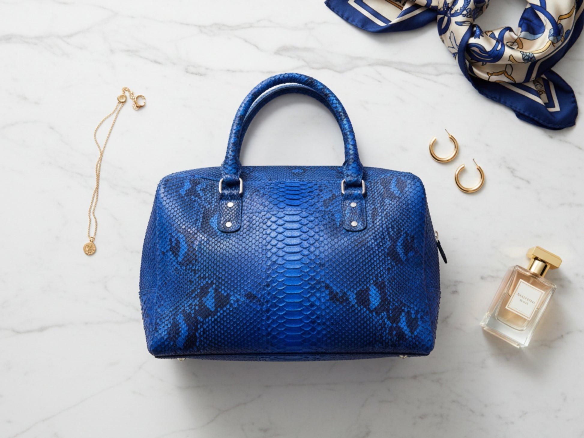 Blue handbag with accessories on a light marble background