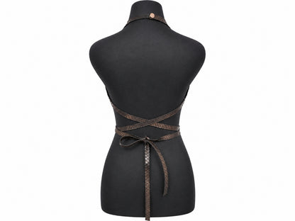 A black dress form mannequin displaying the back of a dark brown woven wrap apron with criss-cross straps and a tie belt.