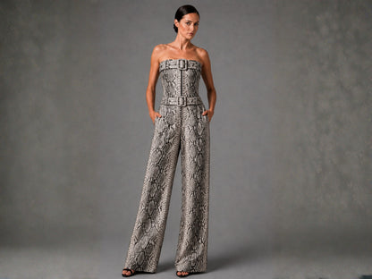A woman models a strapless wide-leg jumpsuit with a snakeskin pattern and matching belt, standing against a textured gray studio backdrop.