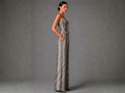 A woman modeling a strapless, floor-length gown with a gray and black snakeskin pattern, standing against a neutral gray studio backdrop.