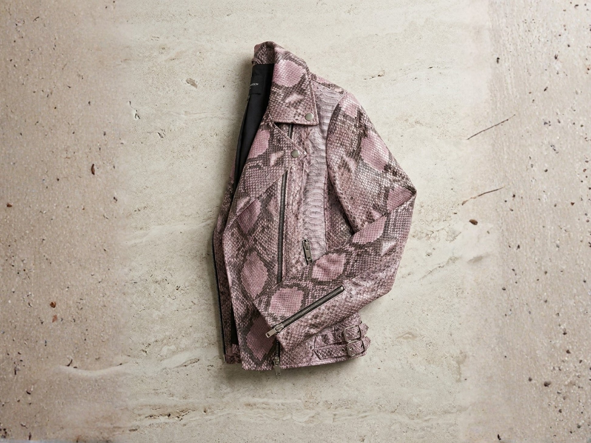 Genuine python leather moto jacket in pink snakeskin pattern hanging against textured wall