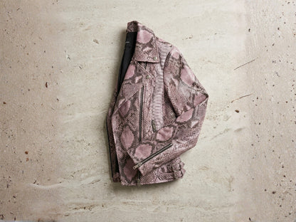 Genuine python leather moto jacket in pink snakeskin pattern hanging against textured wall