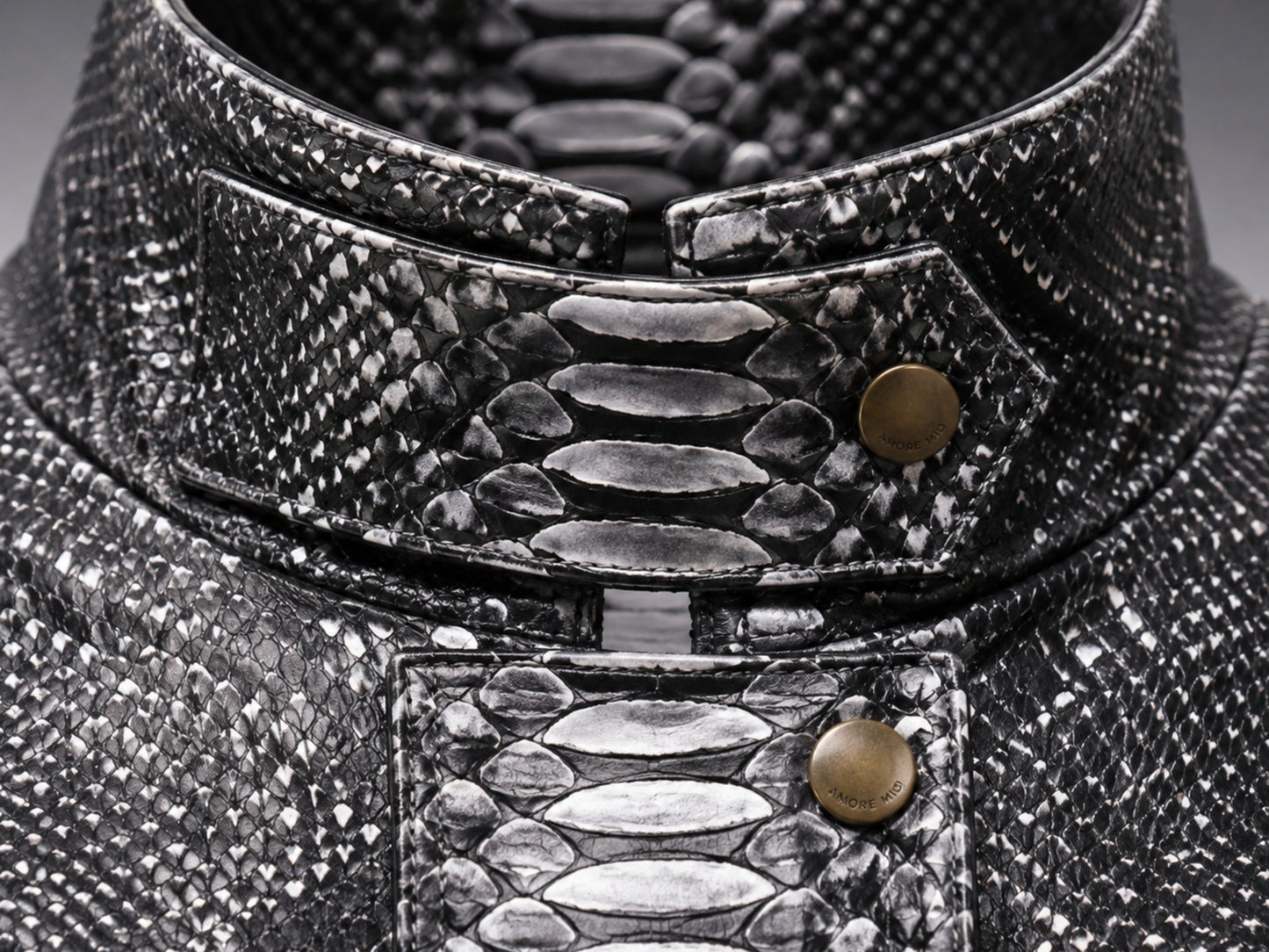 Close-up of a high-collared garment made from textured black and silver snakeskin material, featuring a structured collar with brass-tone snap buttons.