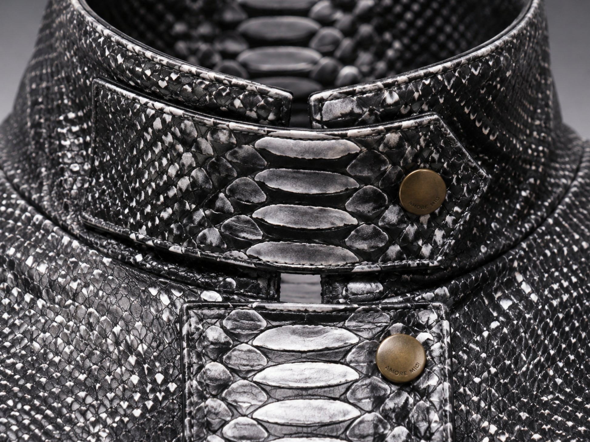 Close-up of a high-collared garment made from textured black and silver snakeskin material, featuring a structured collar with brass-tone snap buttons.