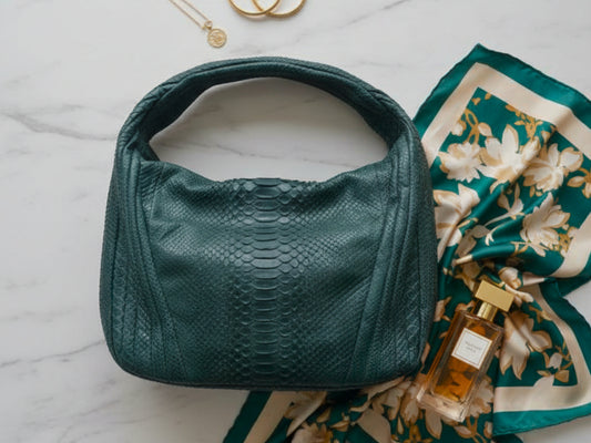 Green handbag with a floral scarf and perfume bottle on a marble surface