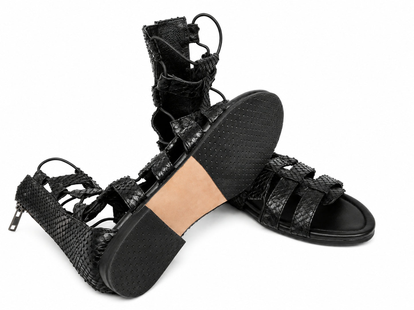 A pair of black woven lace-up sandals with a high heel, shown on a clean white background. One sandal is positioned upright to display the side profile and lace-up closure, while the other lies on its side to show the textured black sole and tan insole.