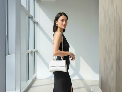 Woman holding a white handbag in an indoor setting with large windows.