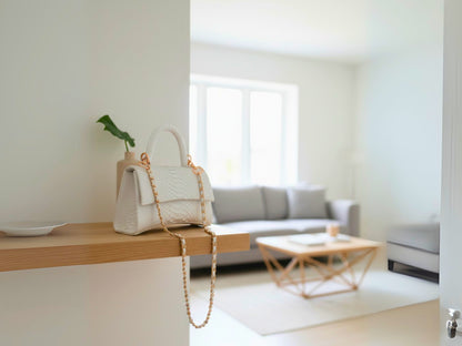 White handbag on a wooden surface with a blurred living room in the background