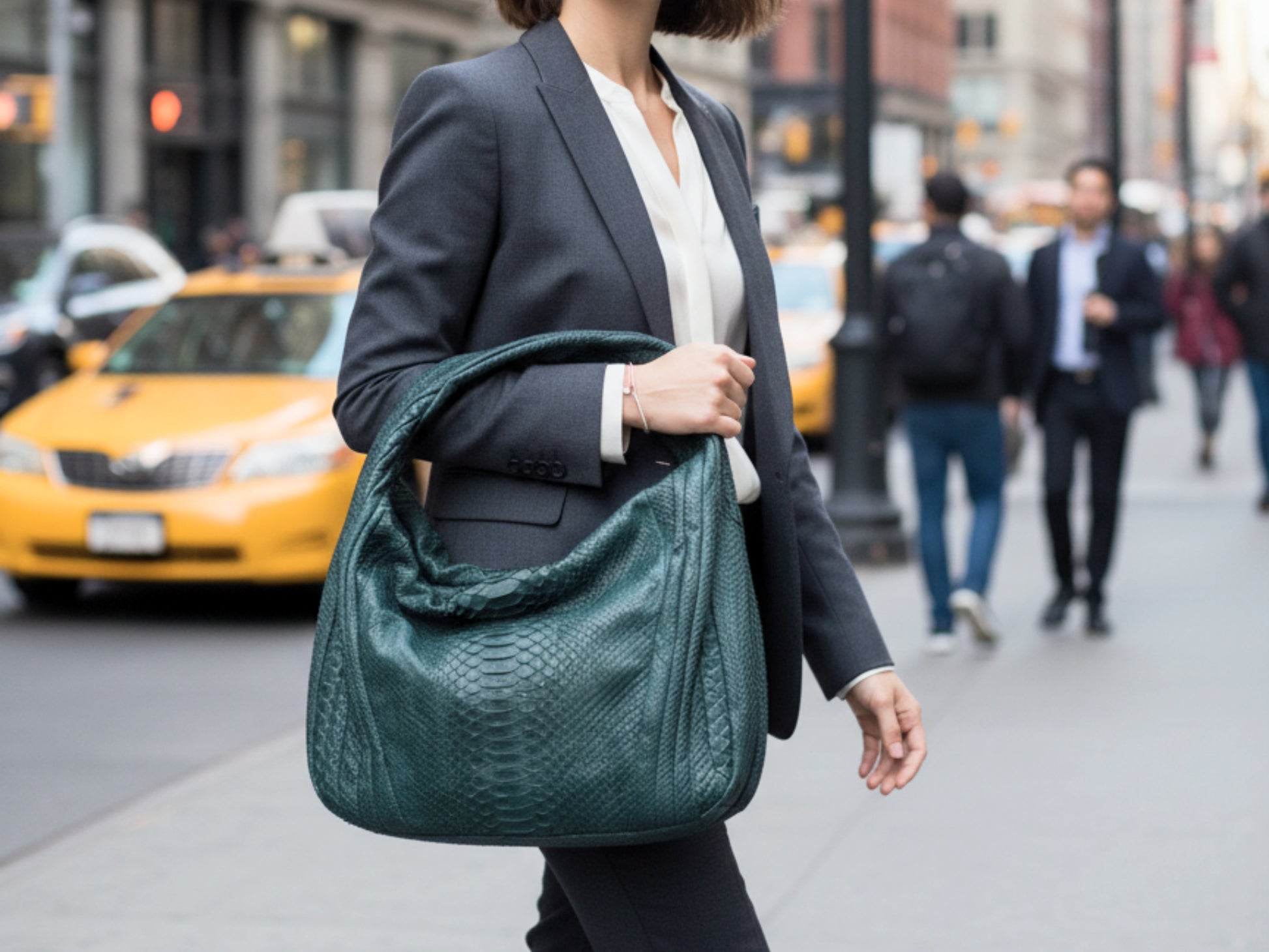 Person holding a green handbag on a city street with taxis in the background