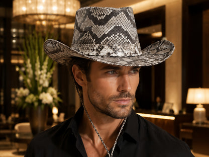 A man wearing a black and white snakeskin-patterned cowboy hat, styled with a silver chain necklace and a black shirt, set against a warm, upscale interior background.