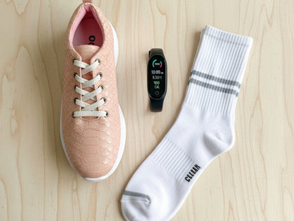 Pink sneaker, black smartwatch, and white socks on a wooden surface