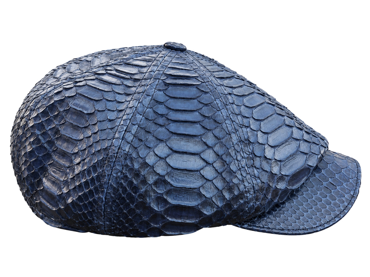 A structured flat cap made of navy blue python skin, showcasing a prominent reptile scale pattern, isolated on a white background.