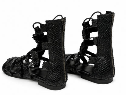 A pair of black snakeskin-textured lace-up sandals with side zippers, shown from a three-quarters angle on a white background.