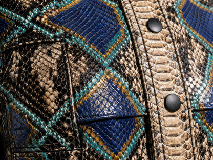 Close-up of a textured leather jacket featuring a geometric diamond pattern with blue, teal, and tan snakeskin print, accented by black snap buttons.