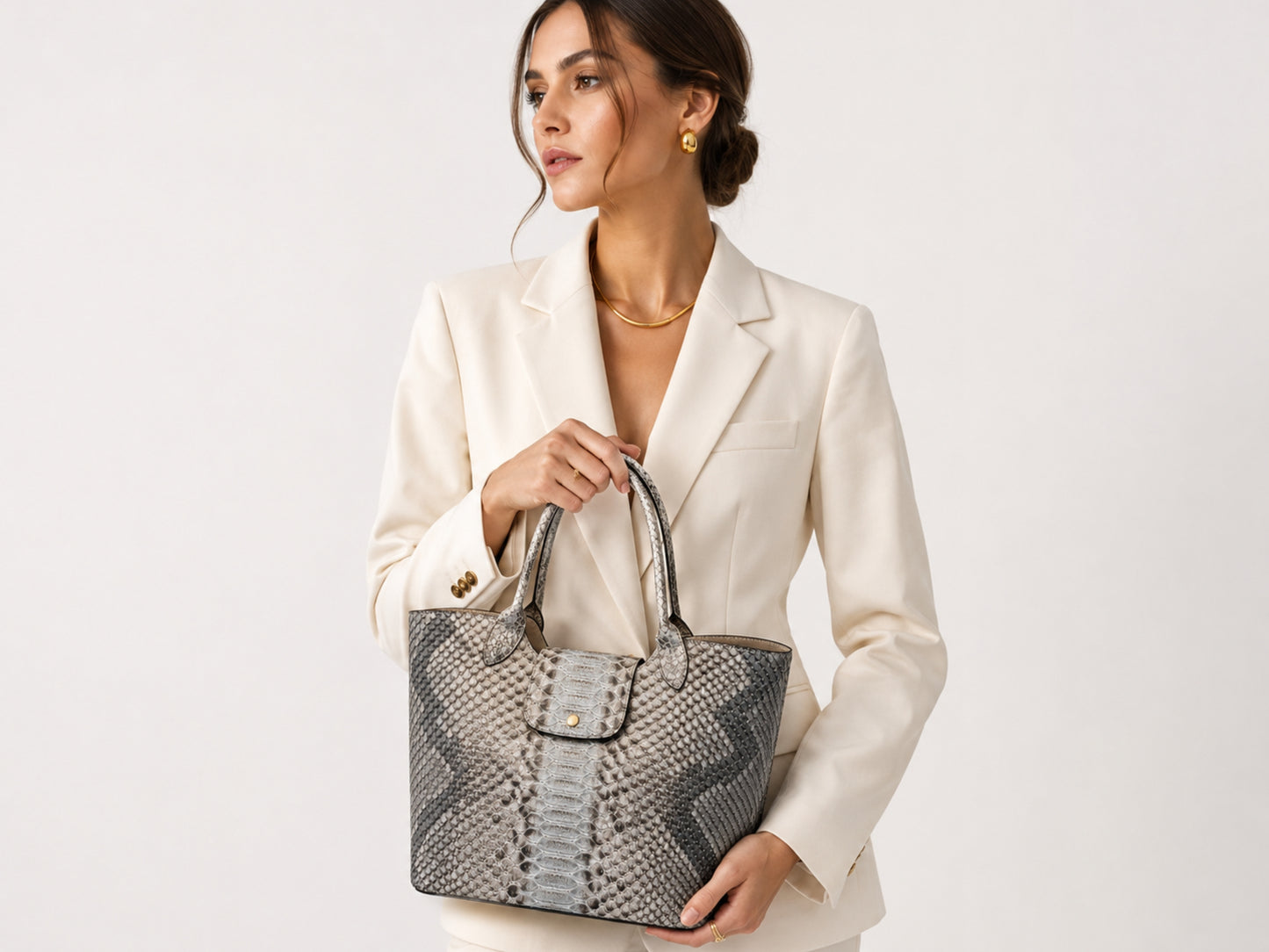 Woman wearing a cream blazer and holding a silver gray genuine python snakeskin shoulder tote bag in luxury studio